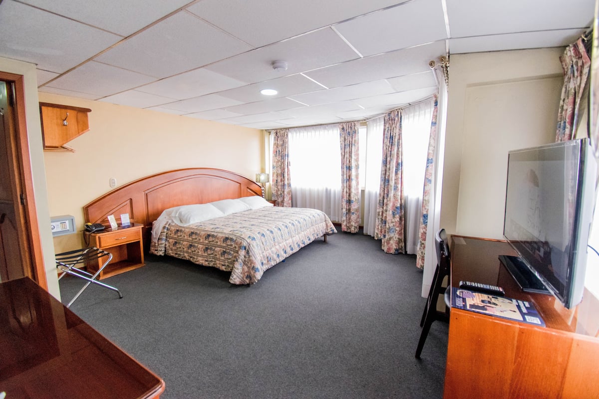 Habitación de hotel con una cama individual, cabecera de madera, televisor de pantalla plana, escritorio con silla y una mesita con bandeja.