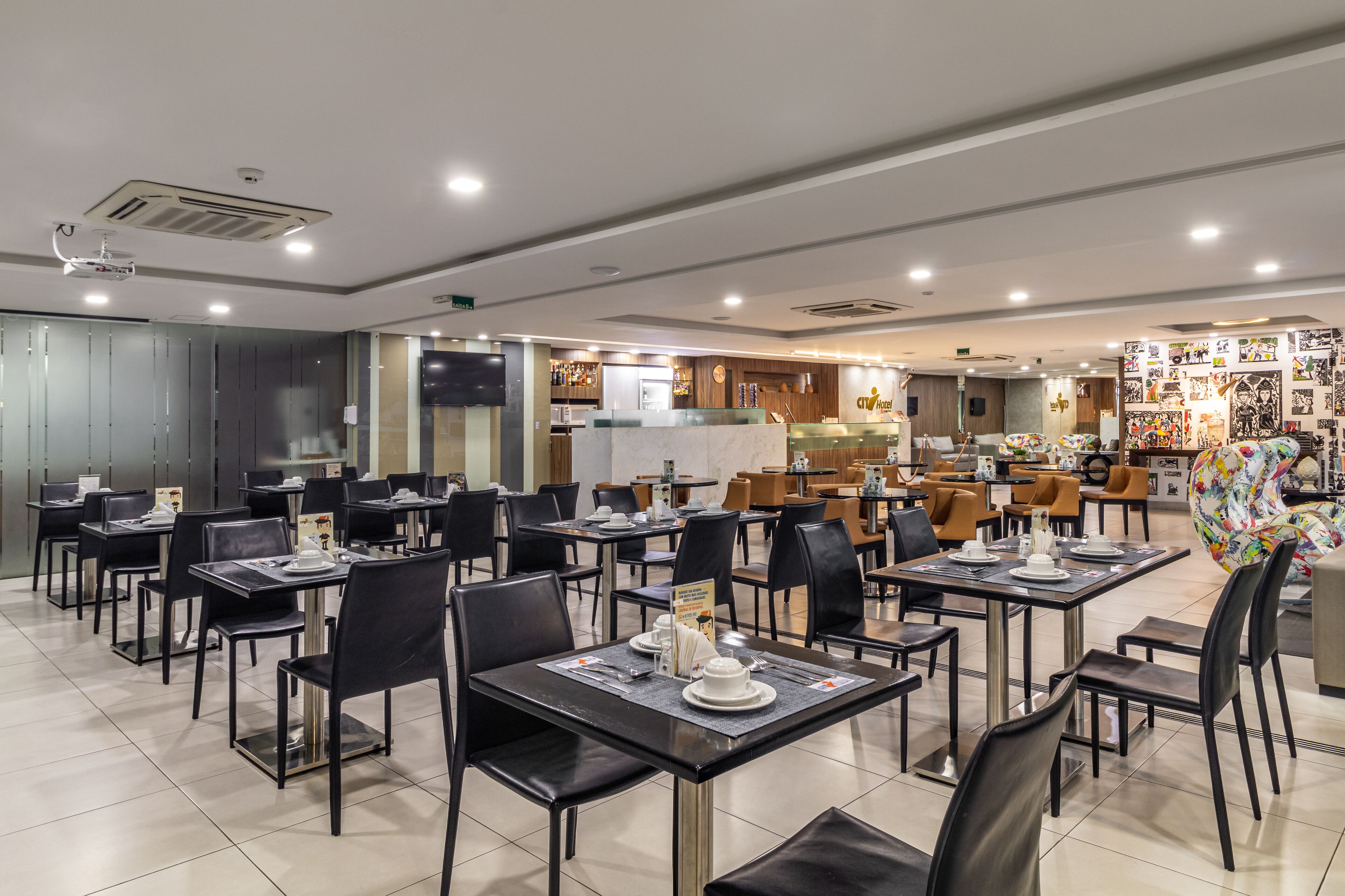 A modern restaurant with multiple dining tables and chairs, a kitchen area, and a wall decorated with various items.