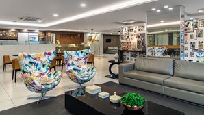 Un moderno vestíbulo de hotel con zona de bar, dos sillas coloridas, un sofá y una mesa de centro con objetos decorativos.