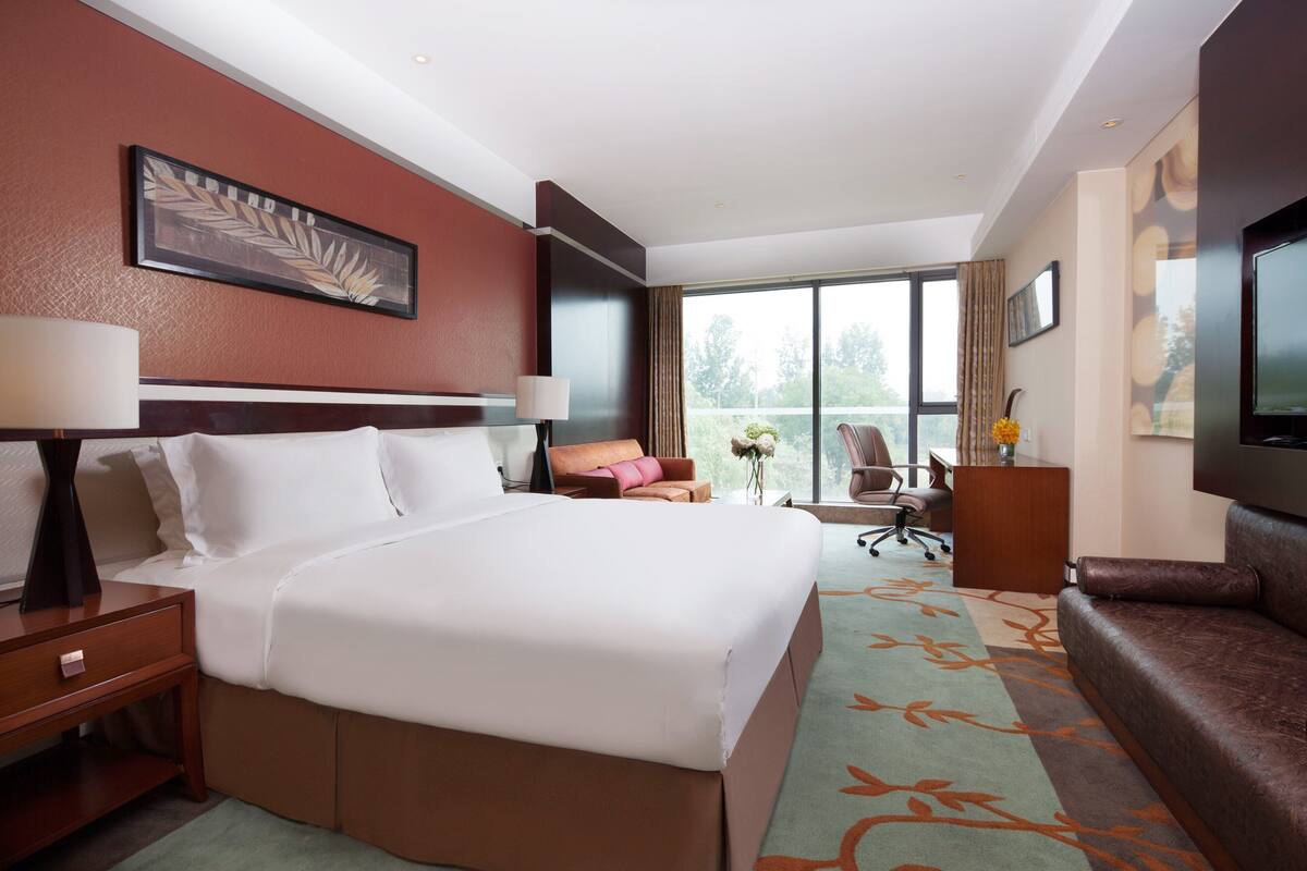 A hotel room with a large bed, a desk, a chair, a sofa, and a TV.