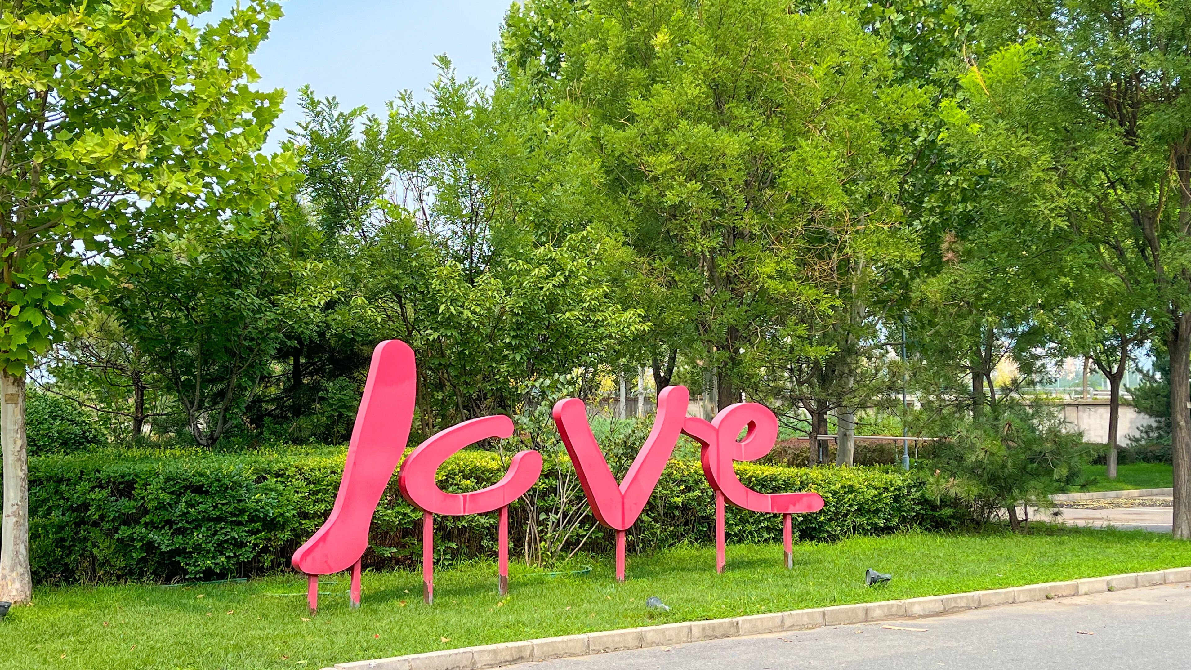 A park with a large pink 'LOVE' sign surrounded by lush green trees and grass.