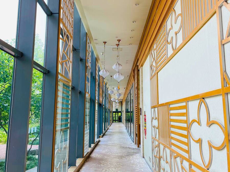Un pasillo con paredes decoradas, ventanas amplias y lámparas colgantes.