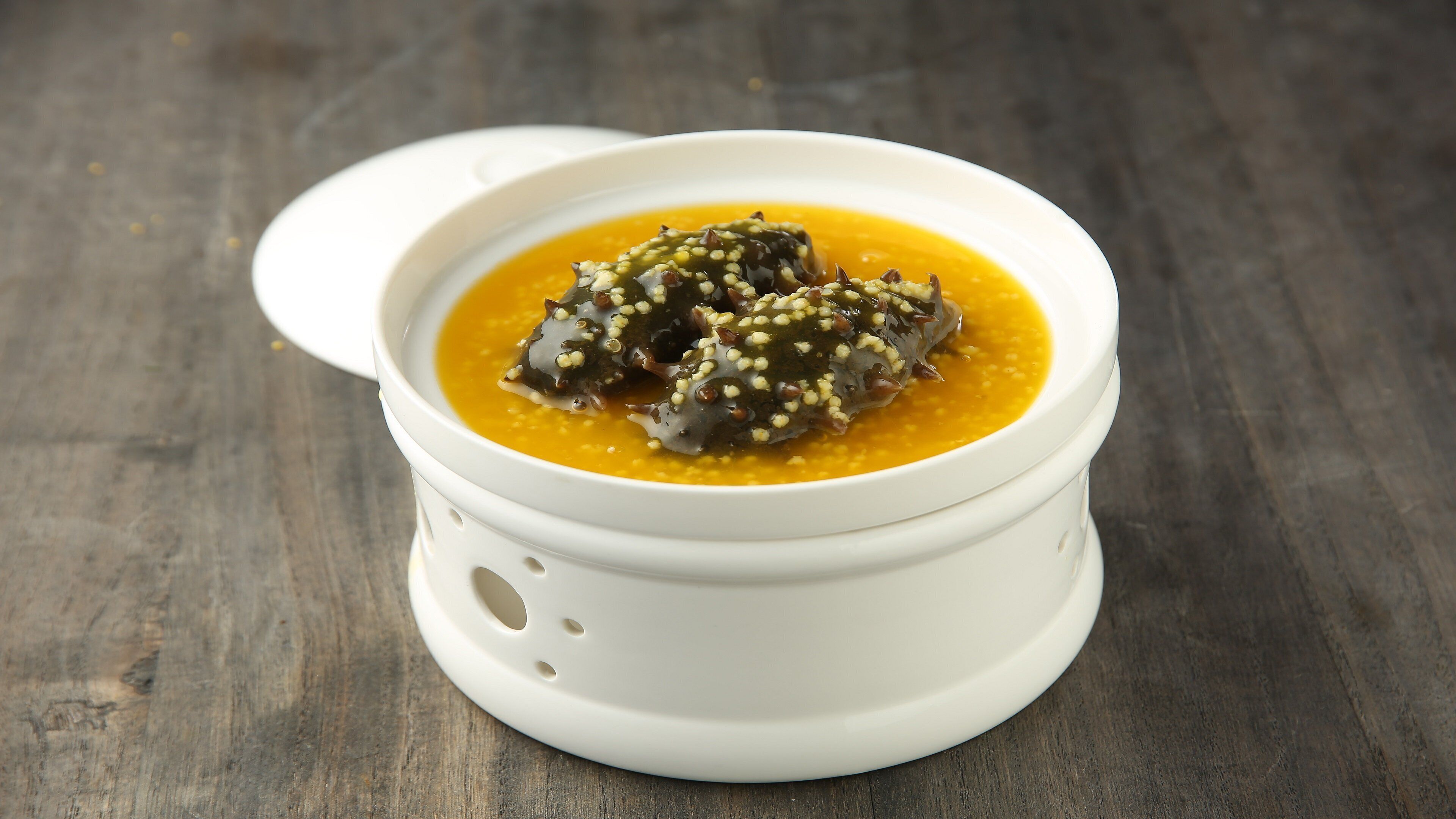 Eine weiße Keramikschale mit Deckel, gefüllt mit gelber Suppe und Seetang-Dekoration, auf einer Holzoberfläche.