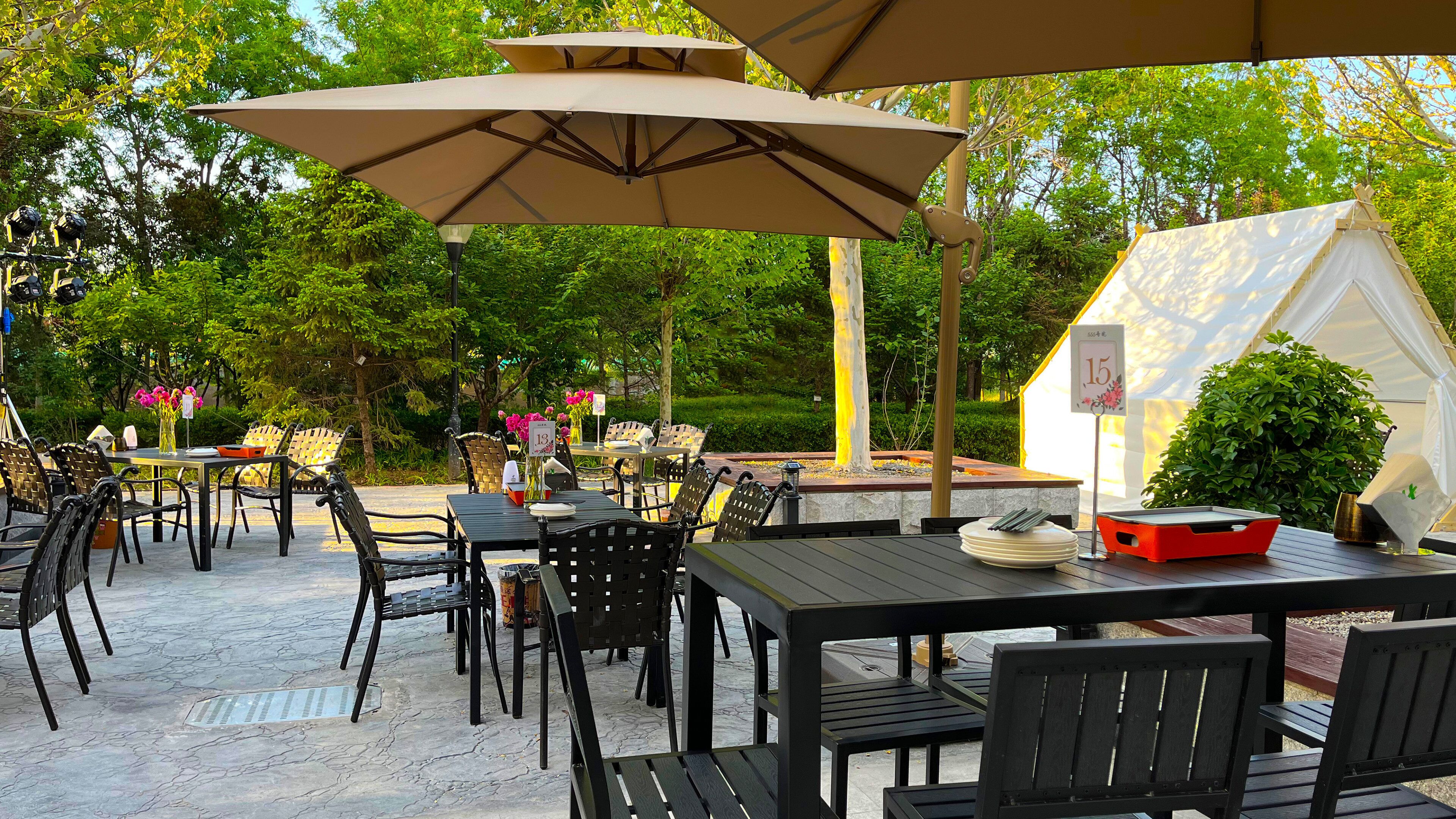Eine Terrasse im Freien mit Tischen und Stühlen unter Sonnenschirmen, umgeben von viel Grün.