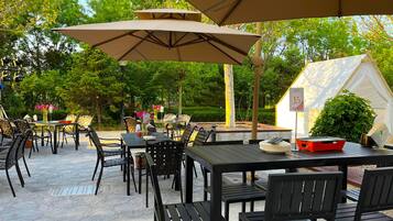 Eine Terrasse im Freien mit Tischen und Stühlen unter Sonnenschirmen, umgeben von viel Grün.