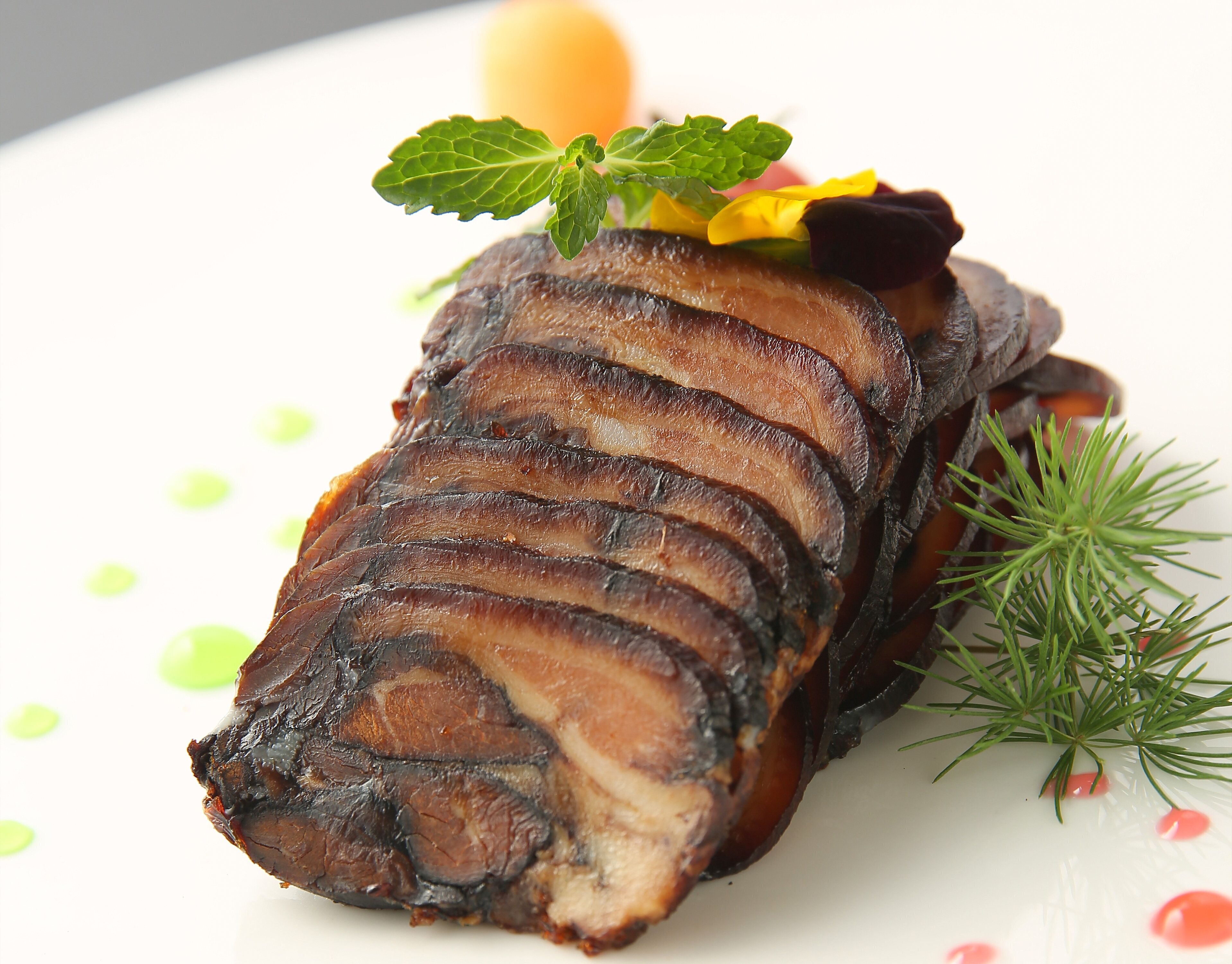 Un plat composé de tranches de viande, garni de menthe et d’une fleur, et servi dans une assiette blanche.