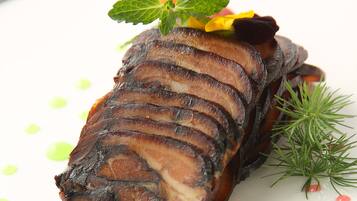 Un plat composé de tranches de viande, garni de menthe et d’une fleur, et servi dans une assiette blanche.