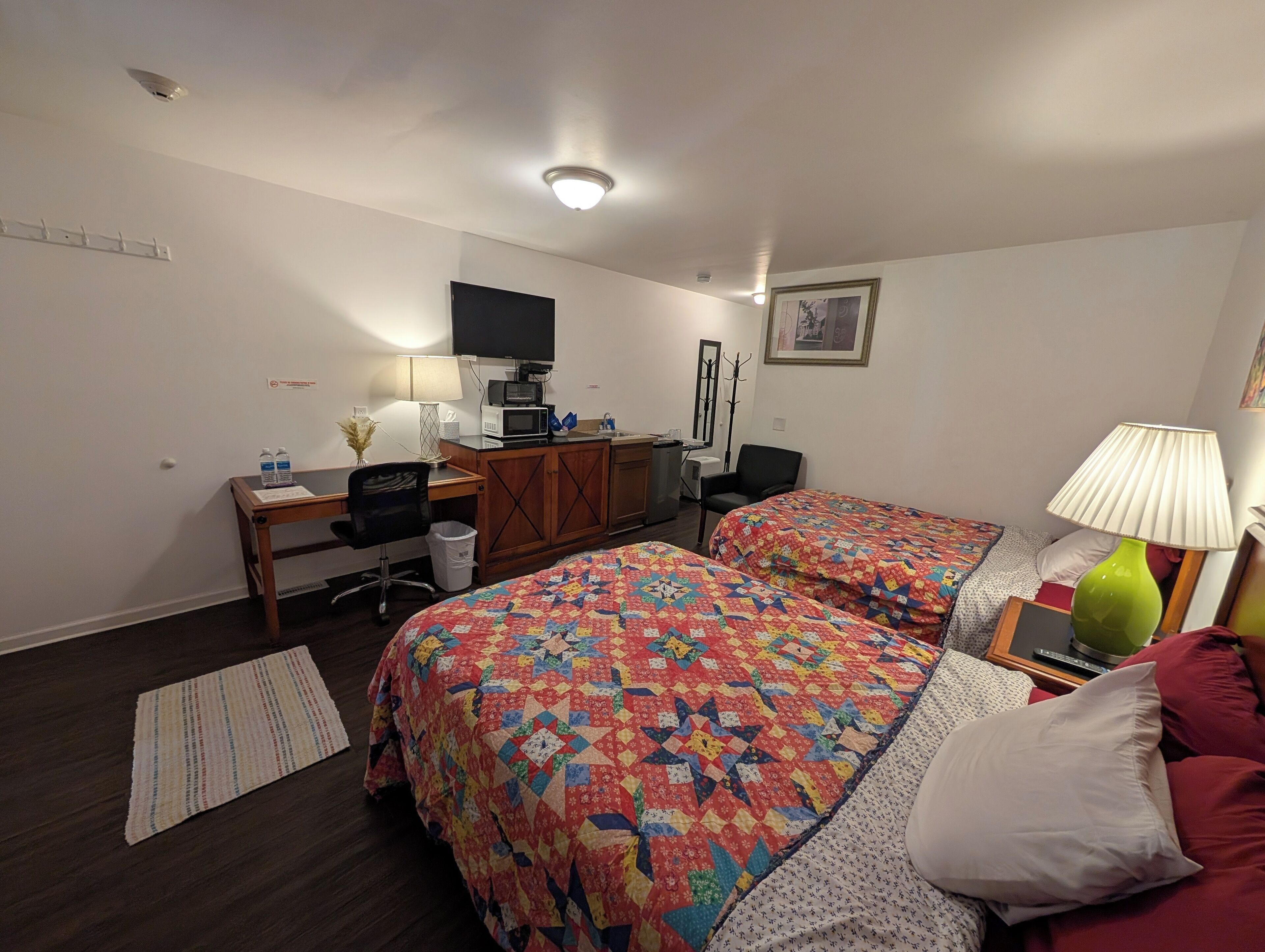 A hotel room with two beds, a desk with a computer, a TV, and a lamp.
