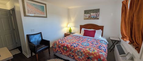 Un dormitorio con cama, una silla, un escritorio, un calentador y dos cuadros en las paredes.