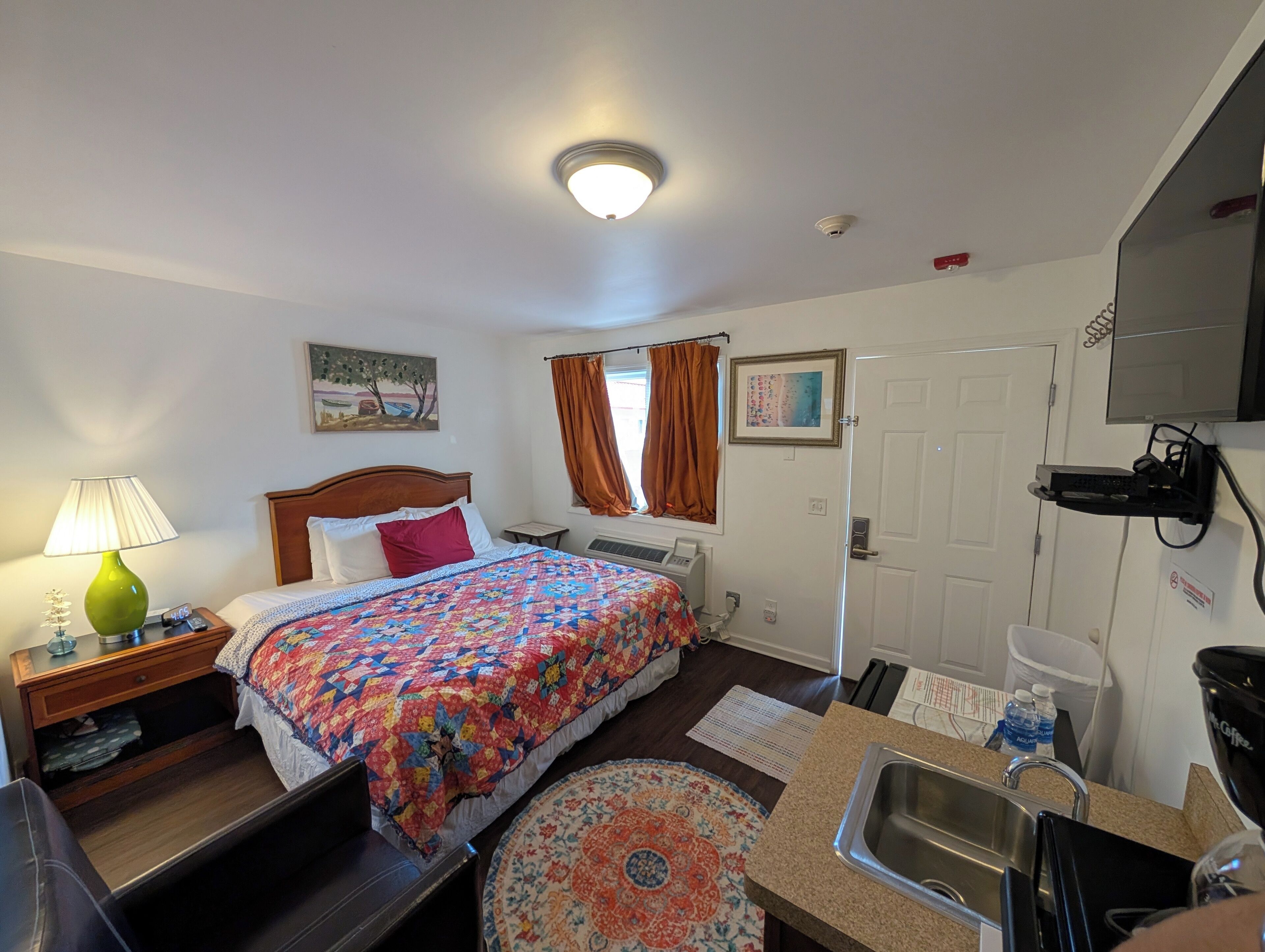 A hotel room with a bed, a desk, a chair, a sink, and a television.
