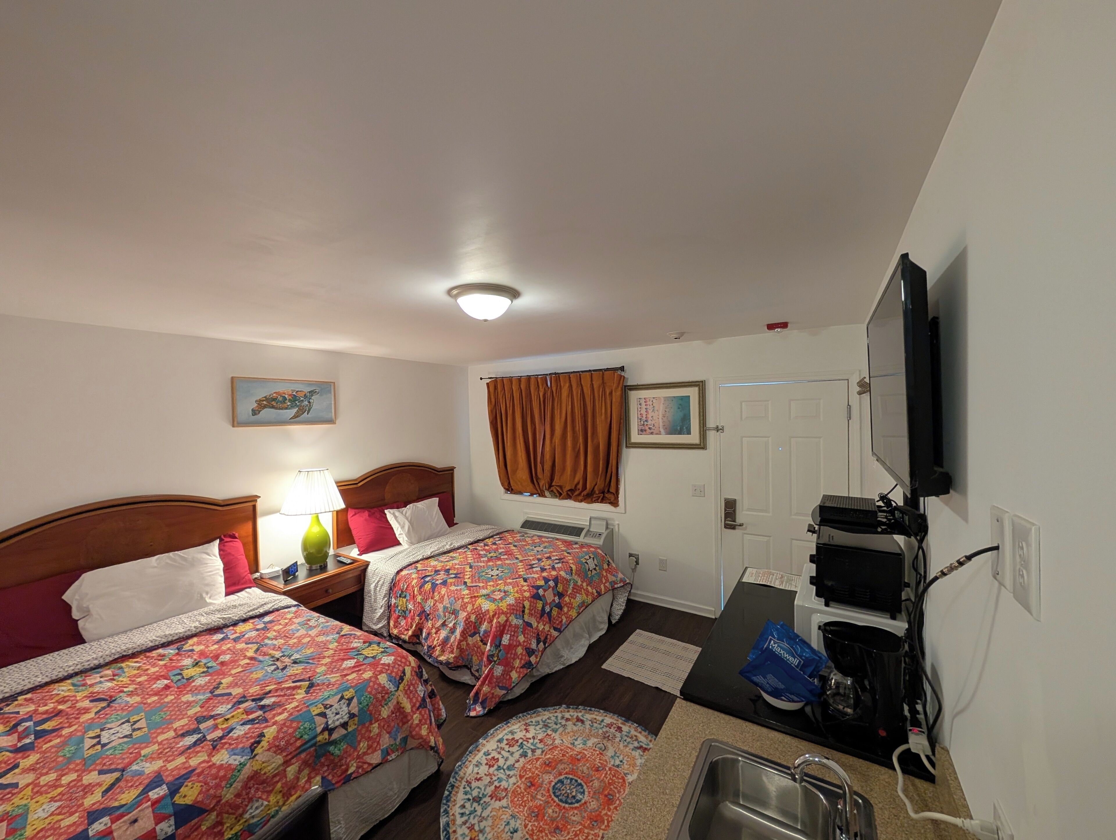 A hotel room with two beds, a television, a desk, and a kitchenette.