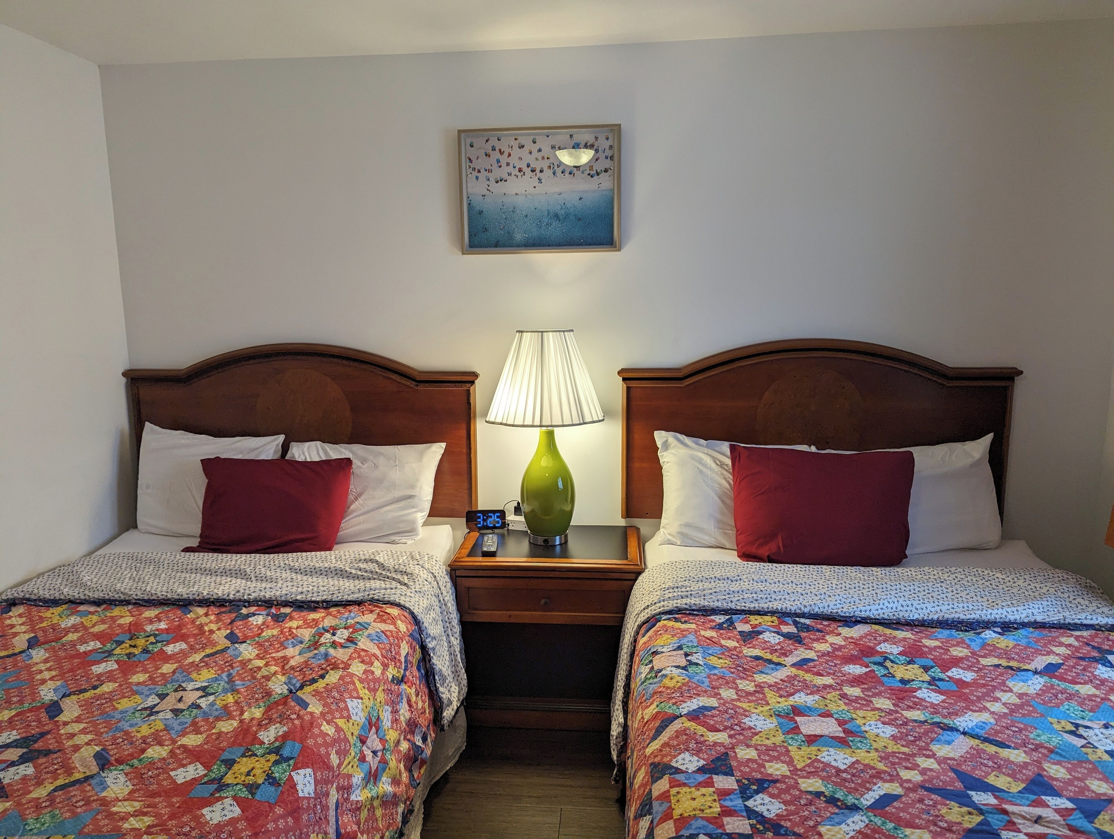 Habitación de hotel con dos camas, cada una con un edredón colorido, una mesita de noche con lámpara y un cuadro en la pared.