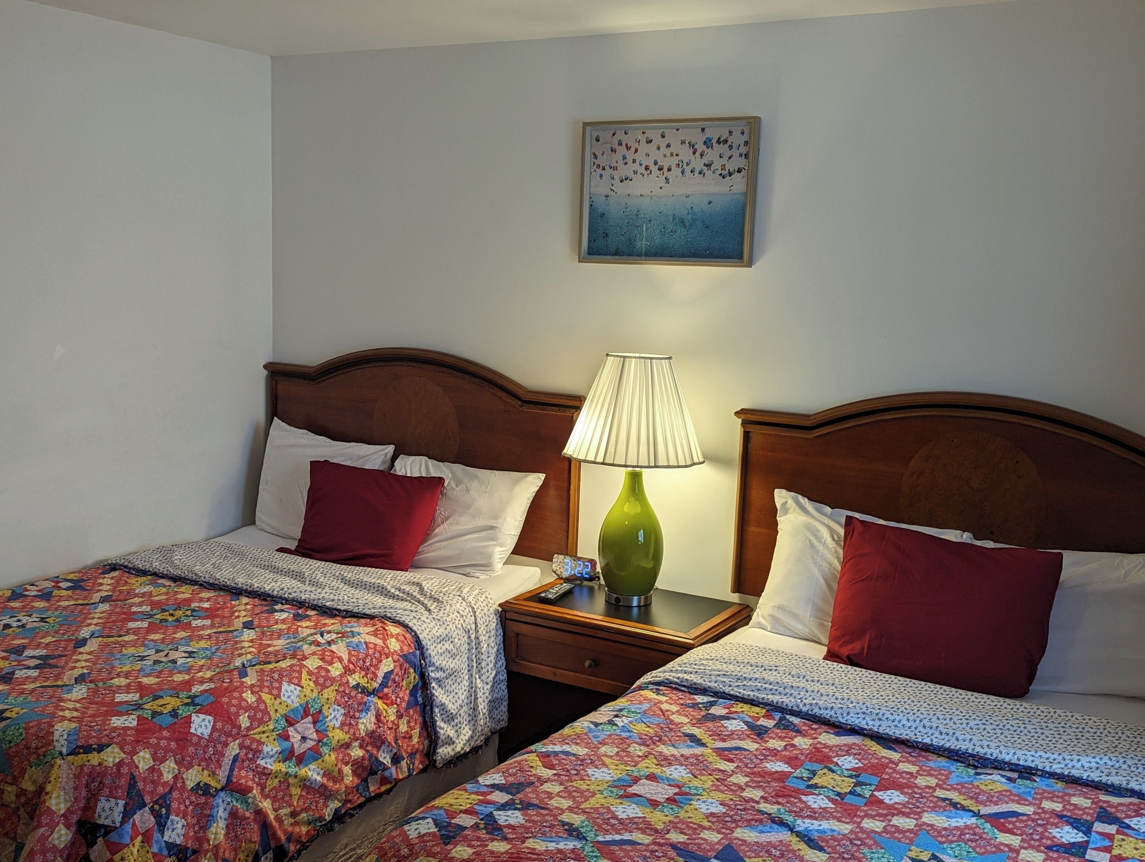 Una habitación de hotel con dos camas, cada una con un edredón colorido, cabeceros de madera, mesitas de noche con lámparas y un cuadro en la pared.