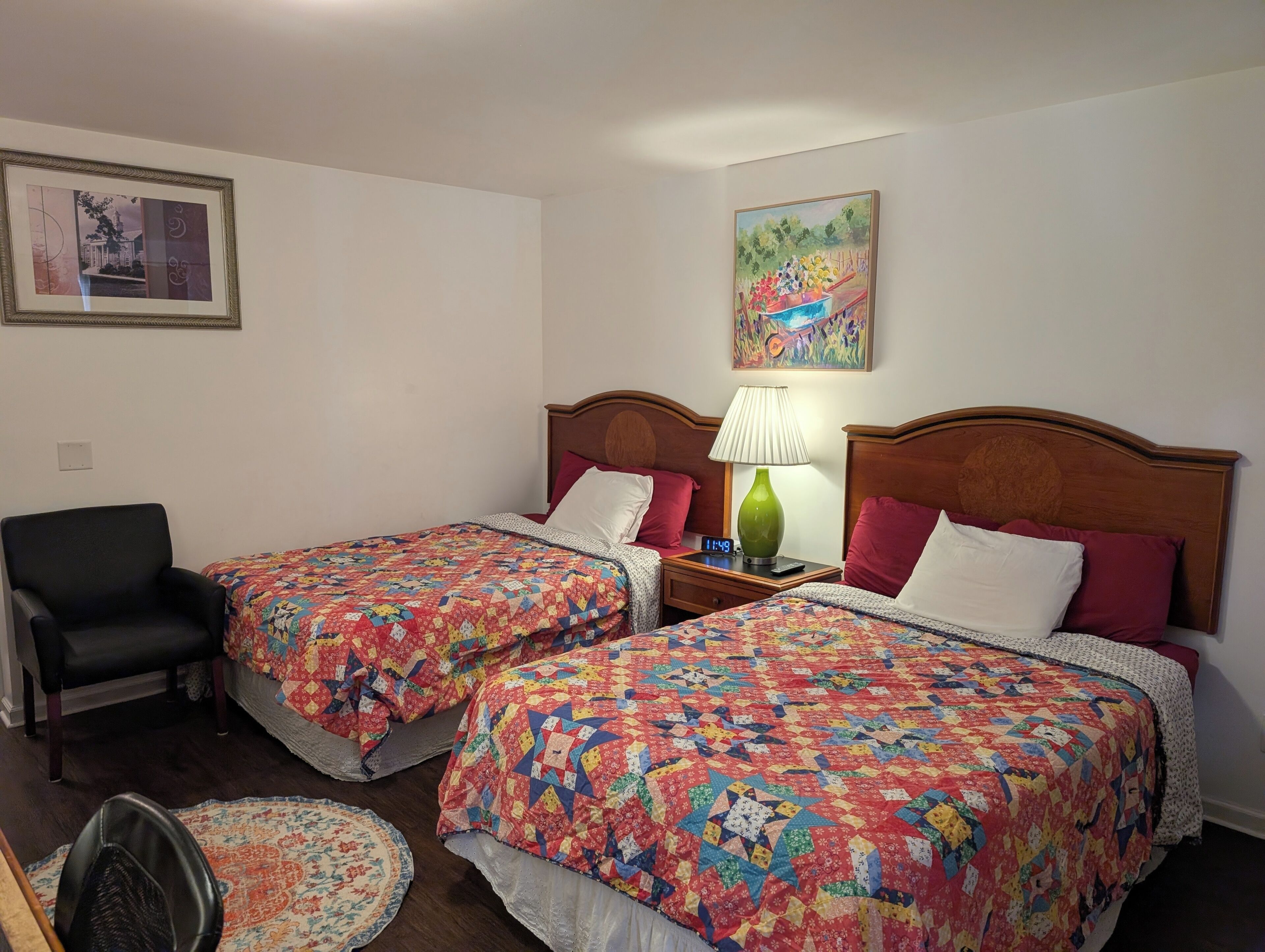 A hotel room with two beds, a chair, a lamp, and a painting on the wall.