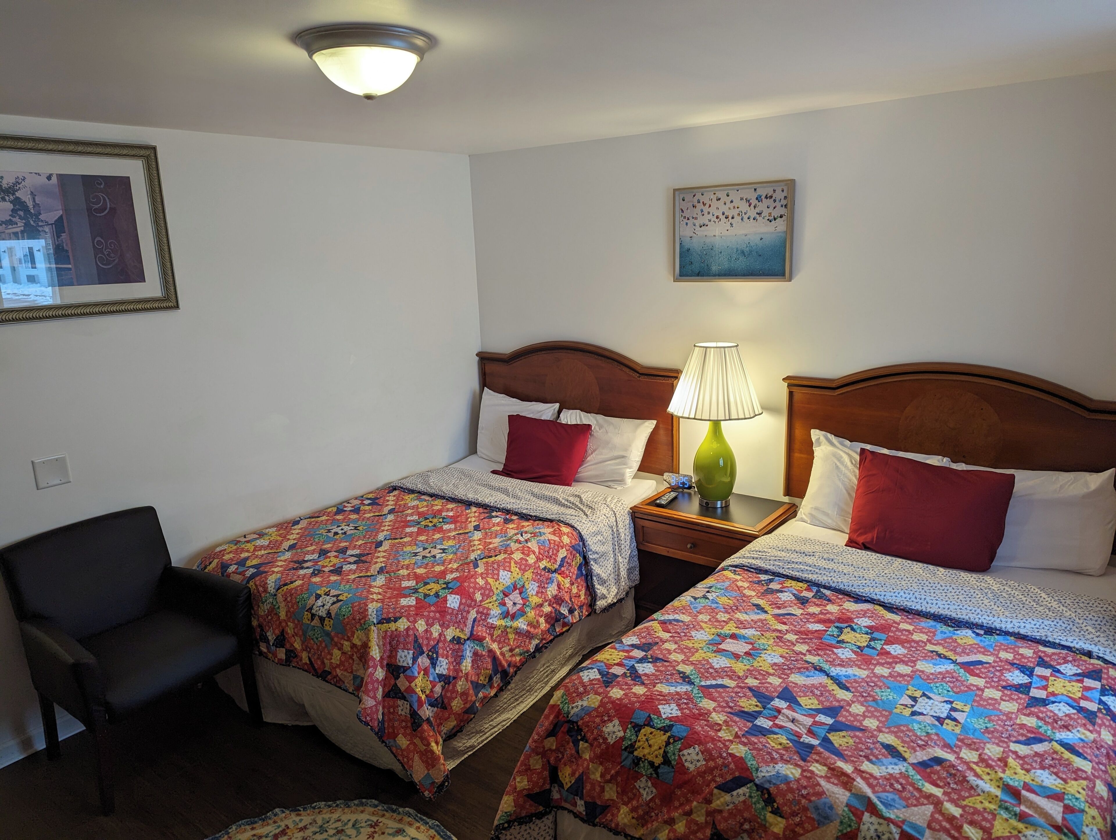 A hotel room with two beds, a chair, a lamp, and a painting on the wall.