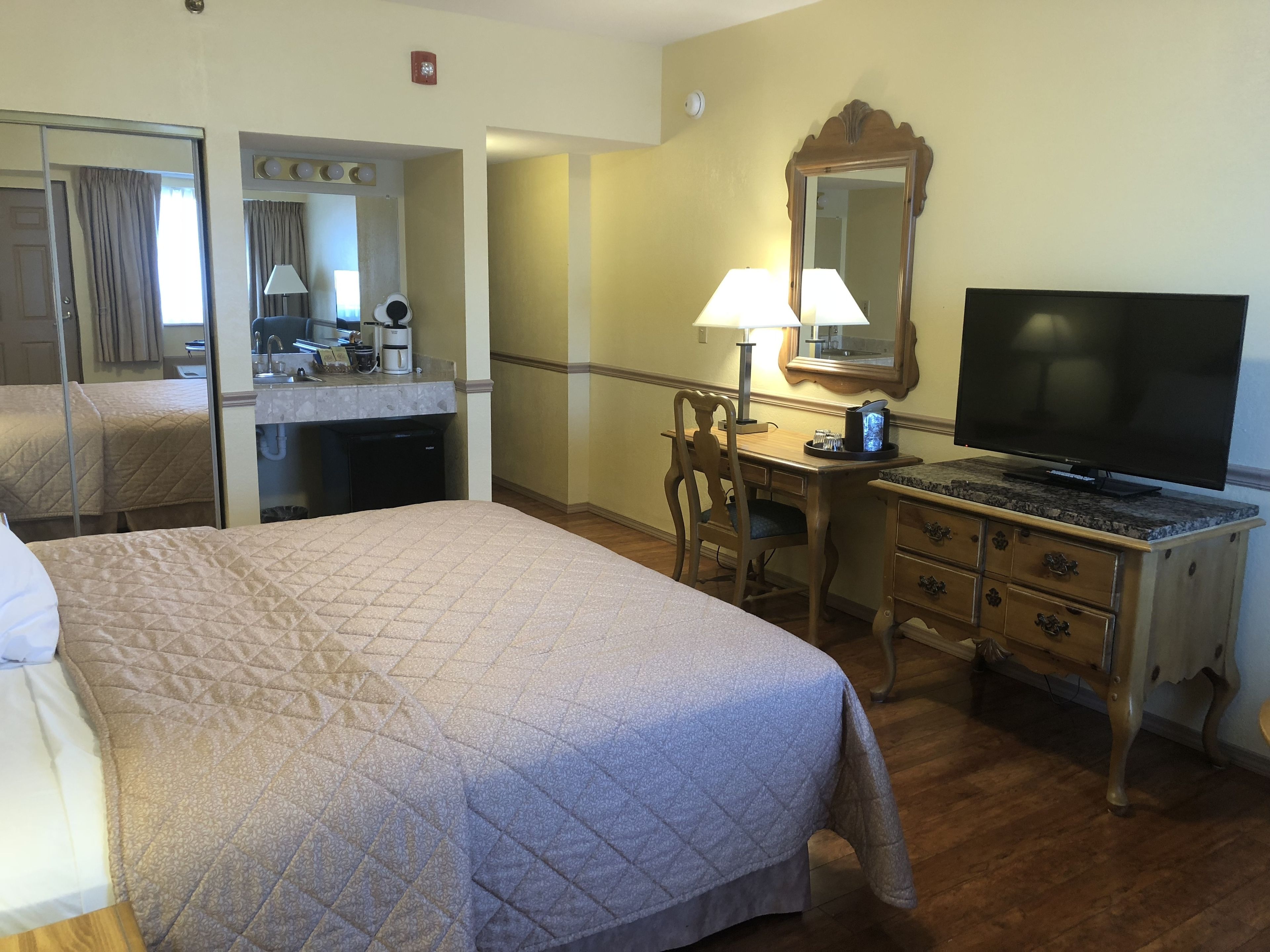 A hotel room with a bed, a desk, a television, and a mirror.