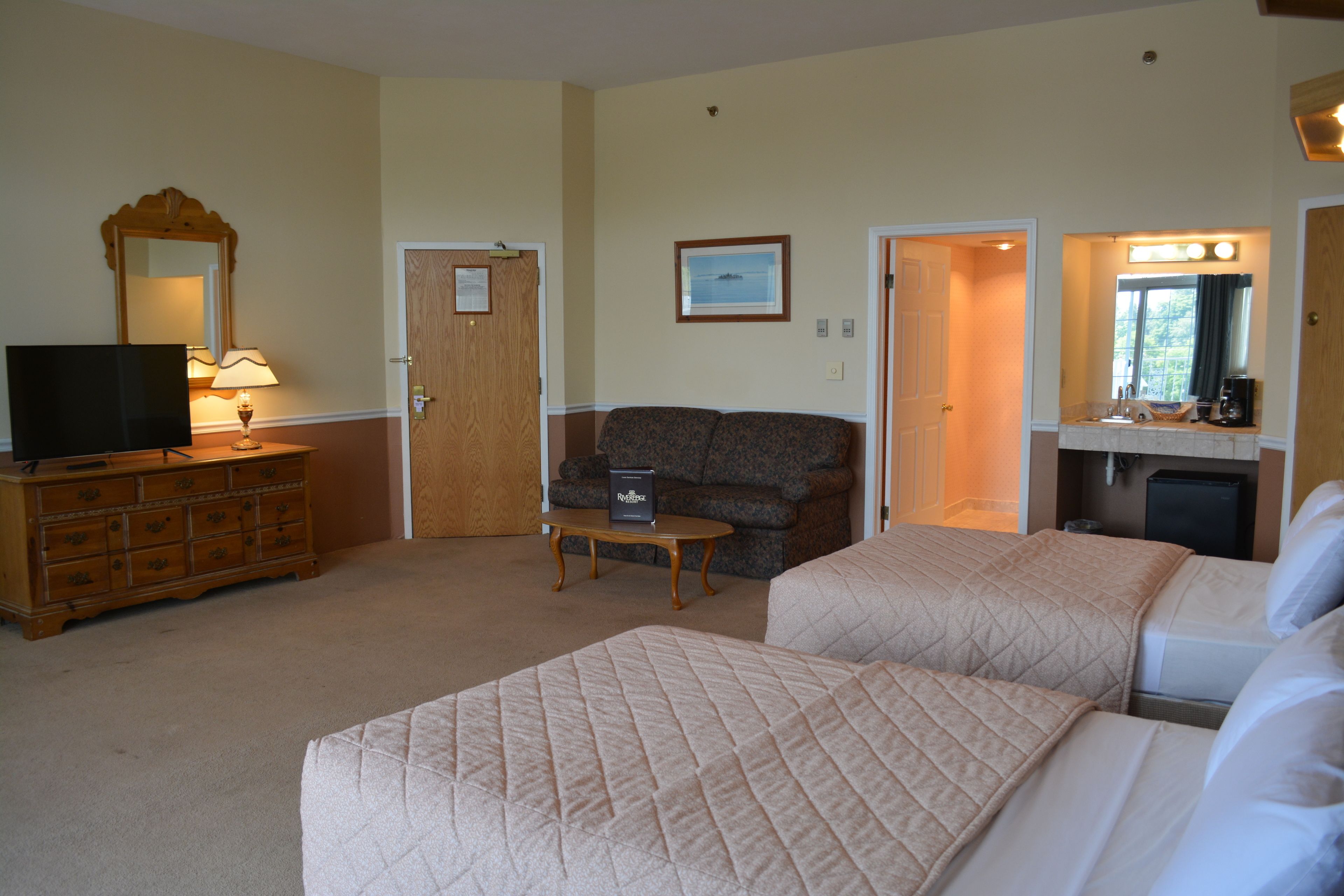 A hotel room with two beds, a TV, a dresser, a sofa, and a small table.