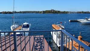 A marina with several boats docked, a clear sky, and a distant shoreline with trees and a castle-like structure. - Riveredge Resort (Alexandria Bay)
