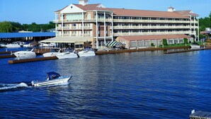 A large waterfront hotel with multiple balconies, a marina with boats, and a covered outdoor seating area. - Riveredge Resort (Alexandria Bay)