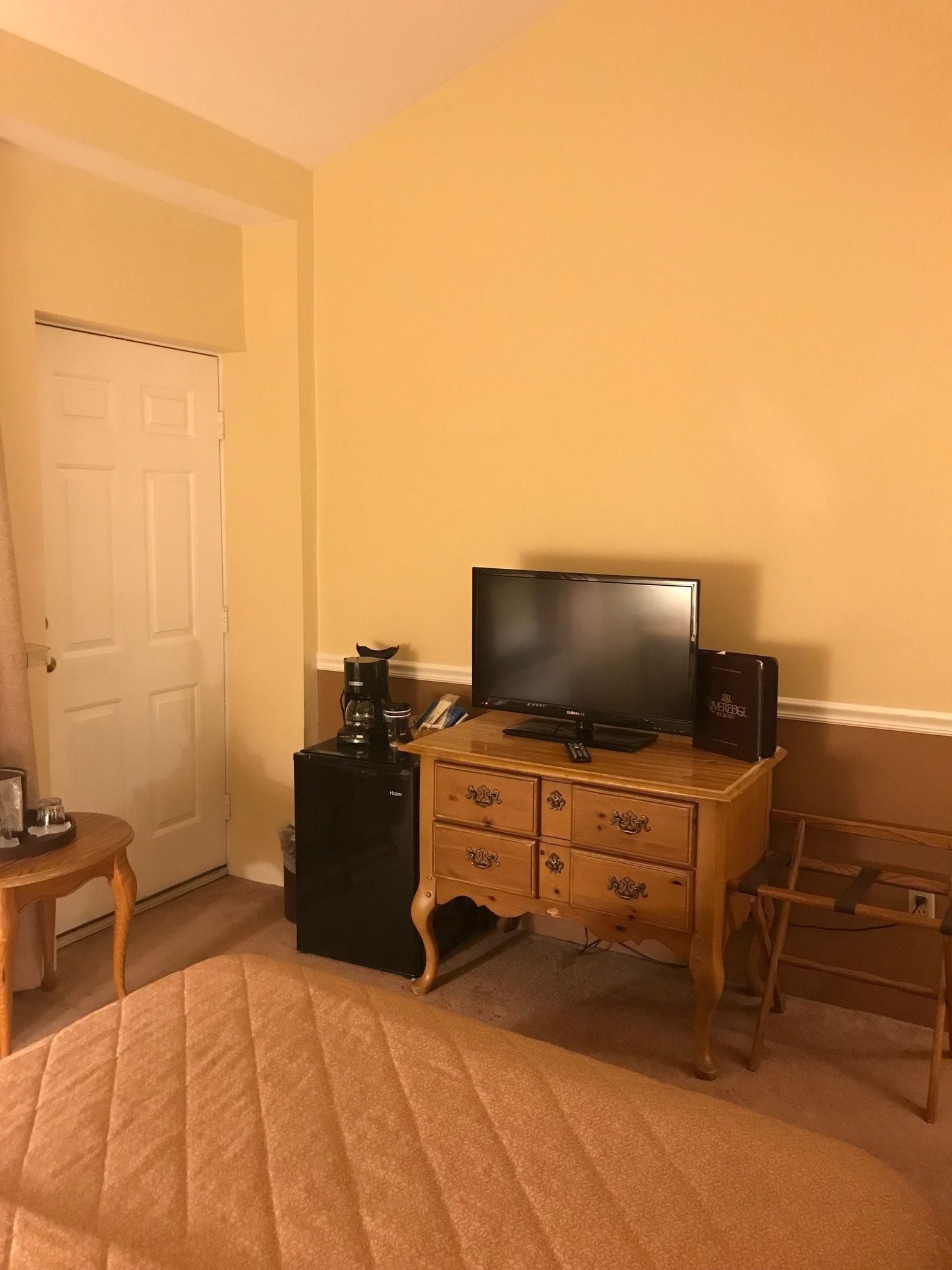 A hotel room with a bed, a wooden dresser, a television, a coffee maker, and a small table.