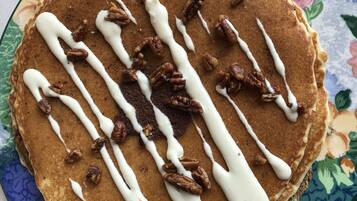 A stack of pancakes with white syrup and pecans on a floral-patterned plate.