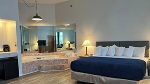 A hotel room with a large bed, a bathroom with a bathtub, a desk, and a TV. - Riveredge Resort (Alexandria Bay)