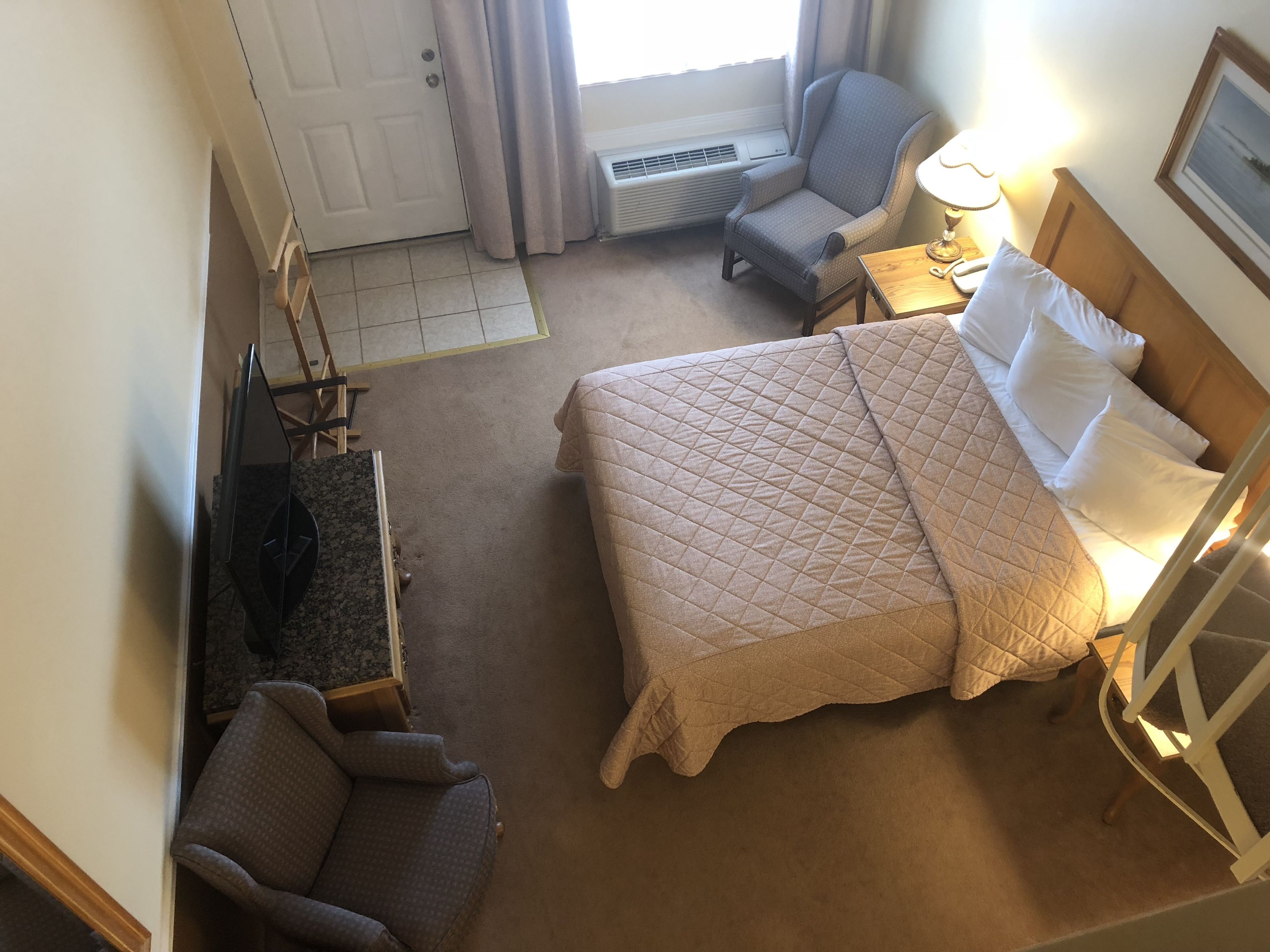 A hotel room with a bed, a chair, a desk, a lamp, and a window with curtains.
