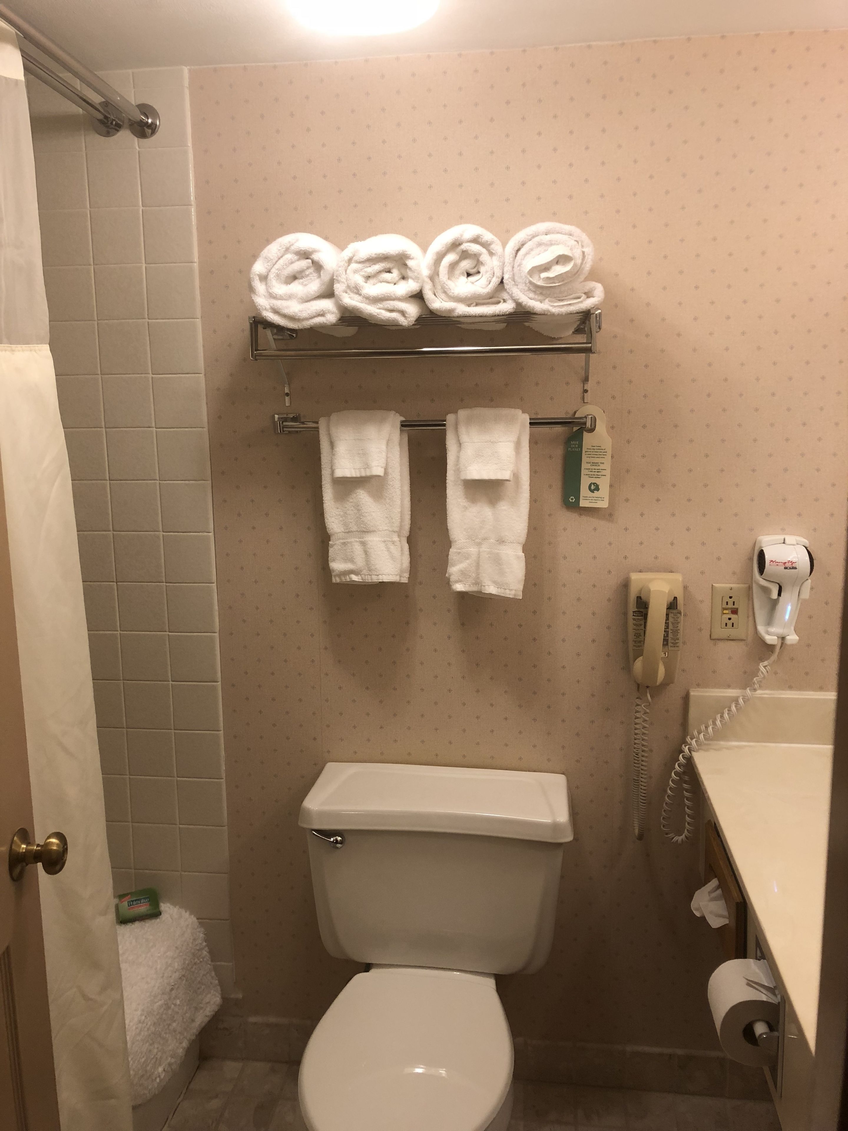 Um banheiro com vaso sanitário, porta-toalhas com toalhas, secador de cabelo e telefone.