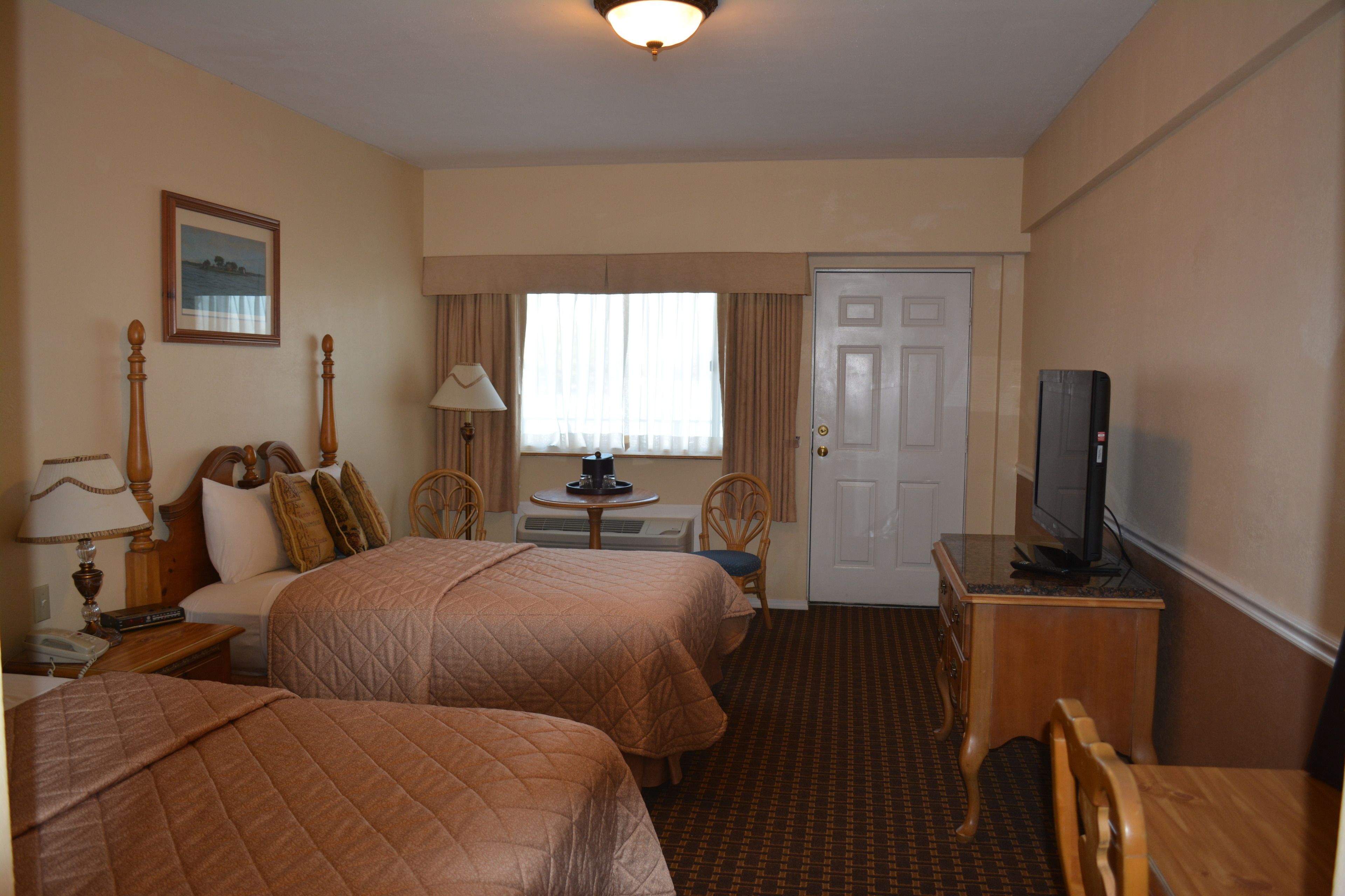 A hotel room with two beds, a television, a desk with a lamp, and a window with curtains.