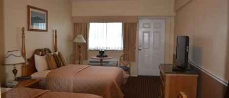 A hotel room with two beds, a television, a desk with a lamp, and a window with curtains.
