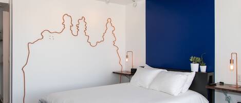 A modern hotel room with a large bed, a wall art installation, bedside tables with lamps, and a blue accent wall.