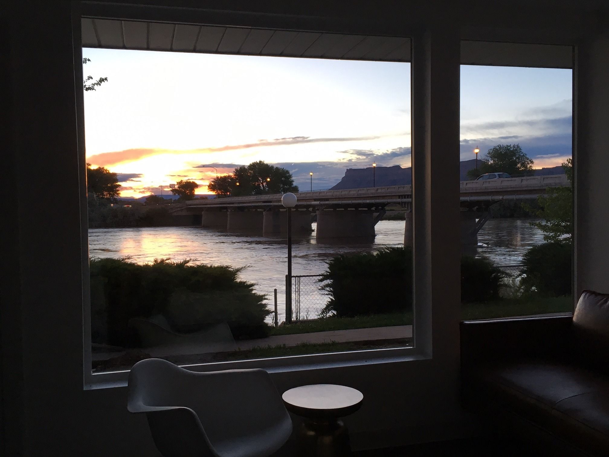Una habitación con un amplio ventanal que da a un río y un puente al atardecer.