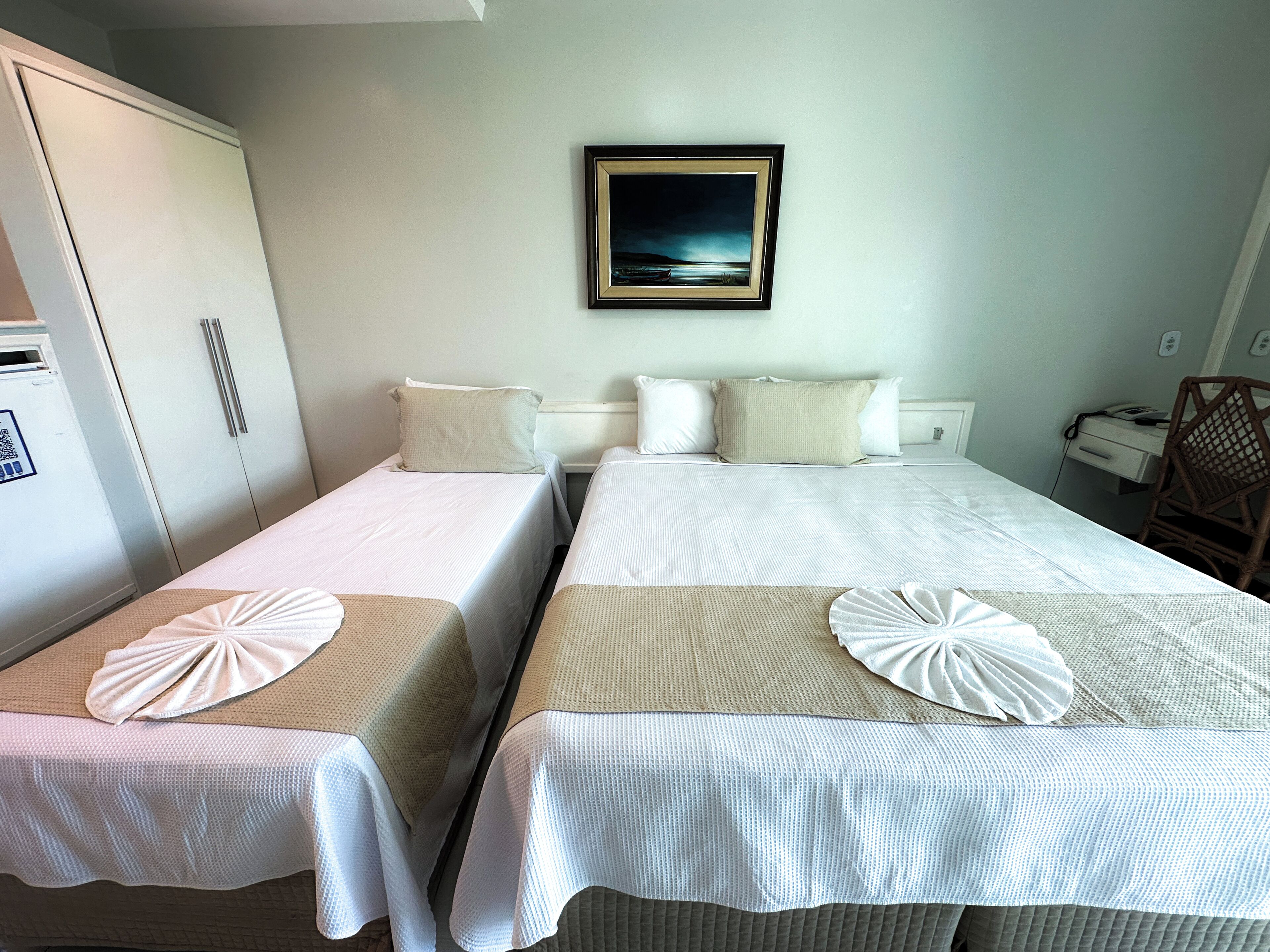 A hotel room with two single beds, a desk, a chair, and a framed picture on the wall.