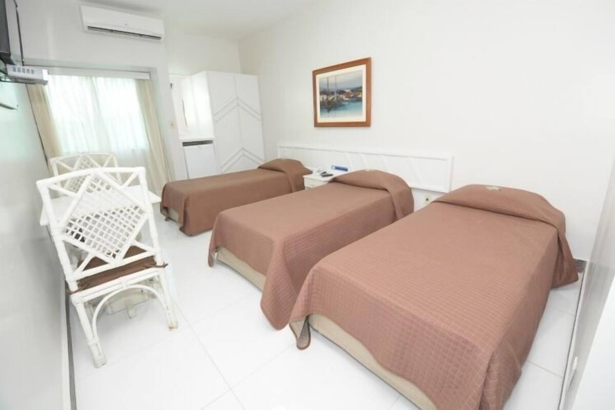 A hotel room with two beds, a white chair, and a picture on the wall.
