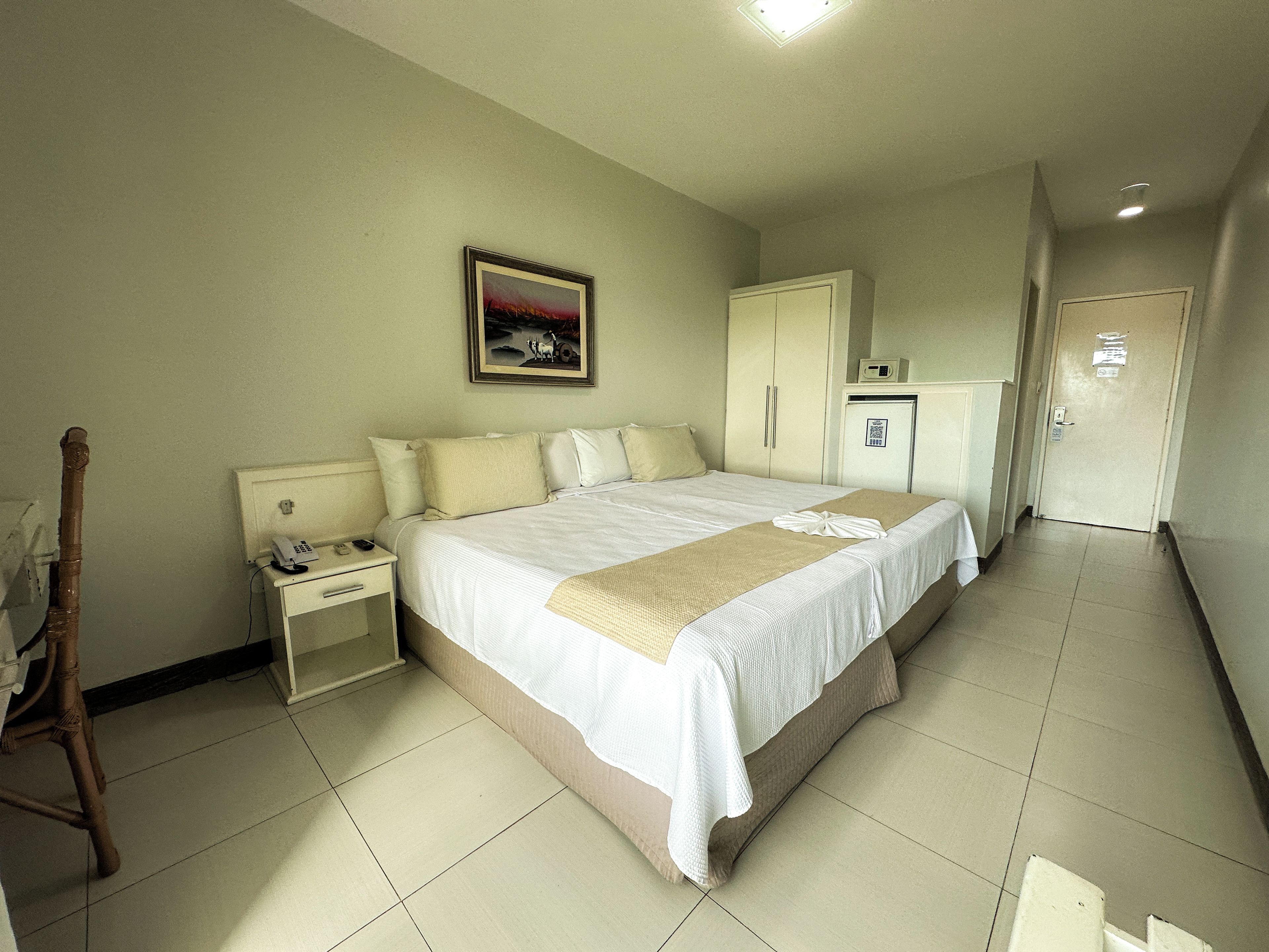 Quarto de hotel com cama, mesa de cabeceira, guarda-roupa, escrivaninha e cadeira.
