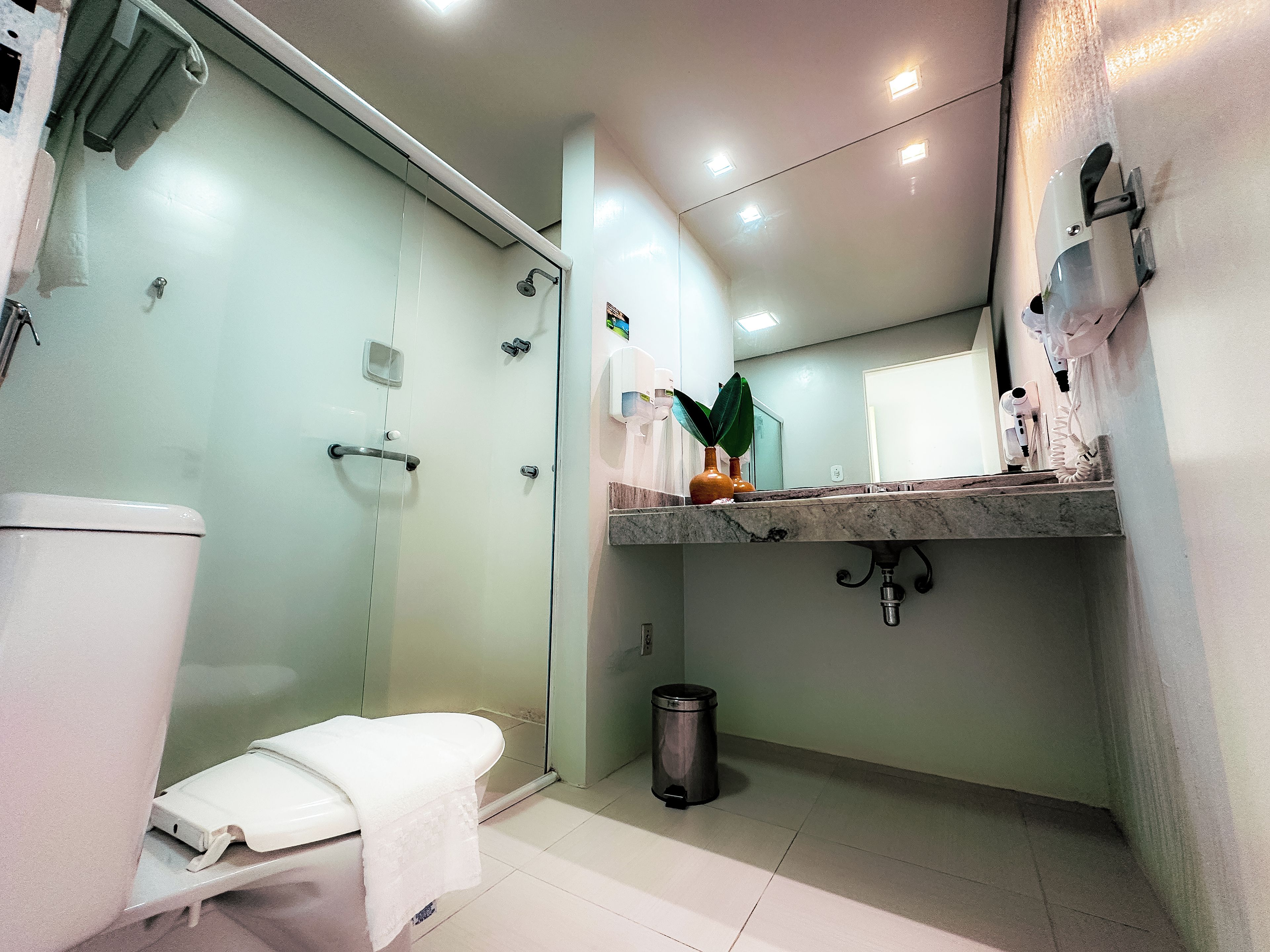 A modern bathroom with a glass-enclosed shower, a toilet, a sink with a marble countertop, and a trash bin.