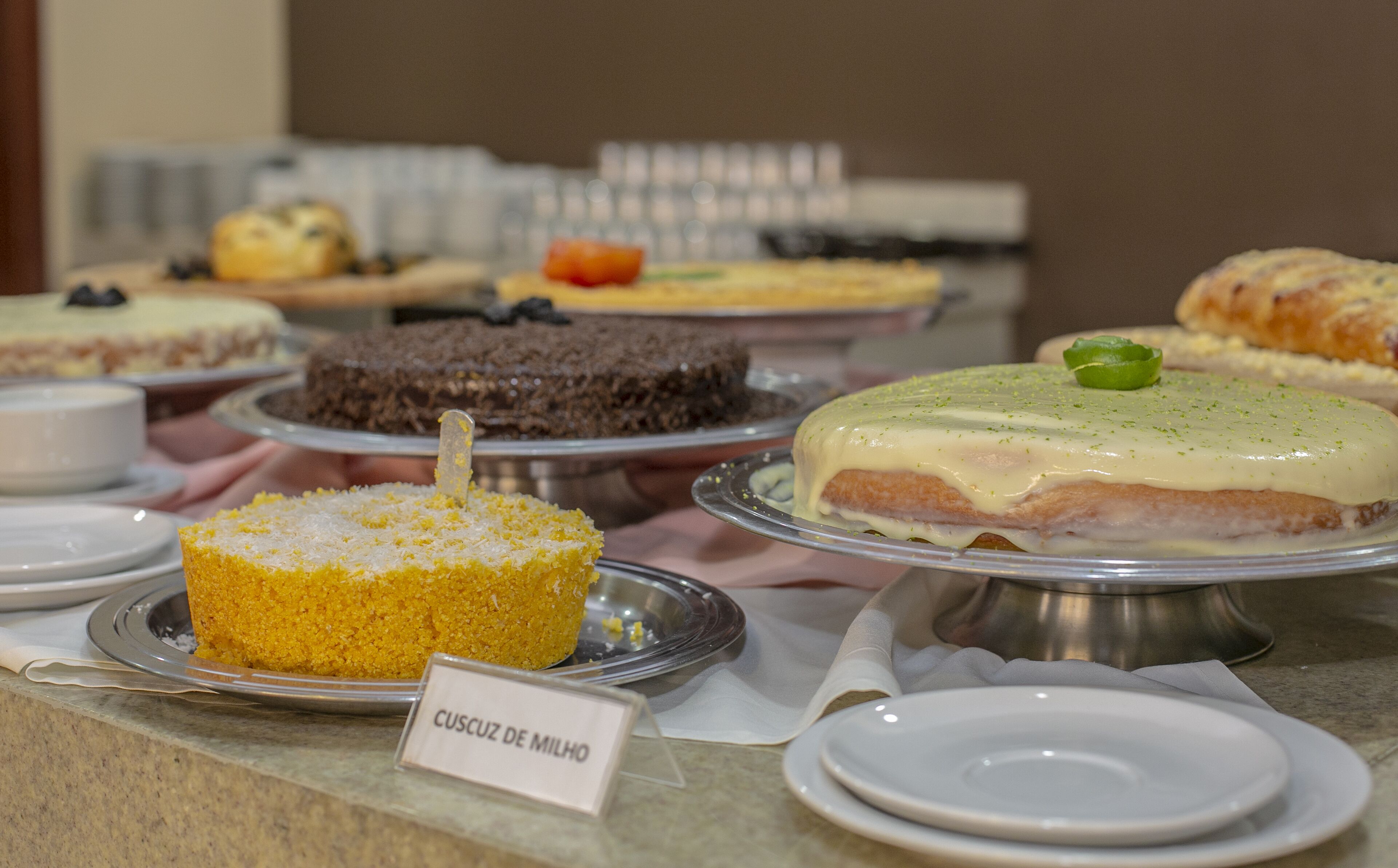 Un buffet con diversi dolci, tra cui una torta con la scritta 'Cuscuz de Milho'.