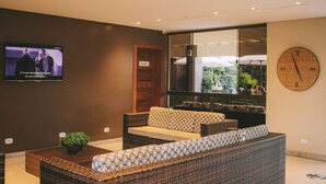 A lobby with wicker furniture, a television, and a clock on the wall. - Safira Praia Hotel (Porto Seguro)