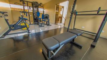 Academia com equipamentos de ginástica, um banco e um espelho.