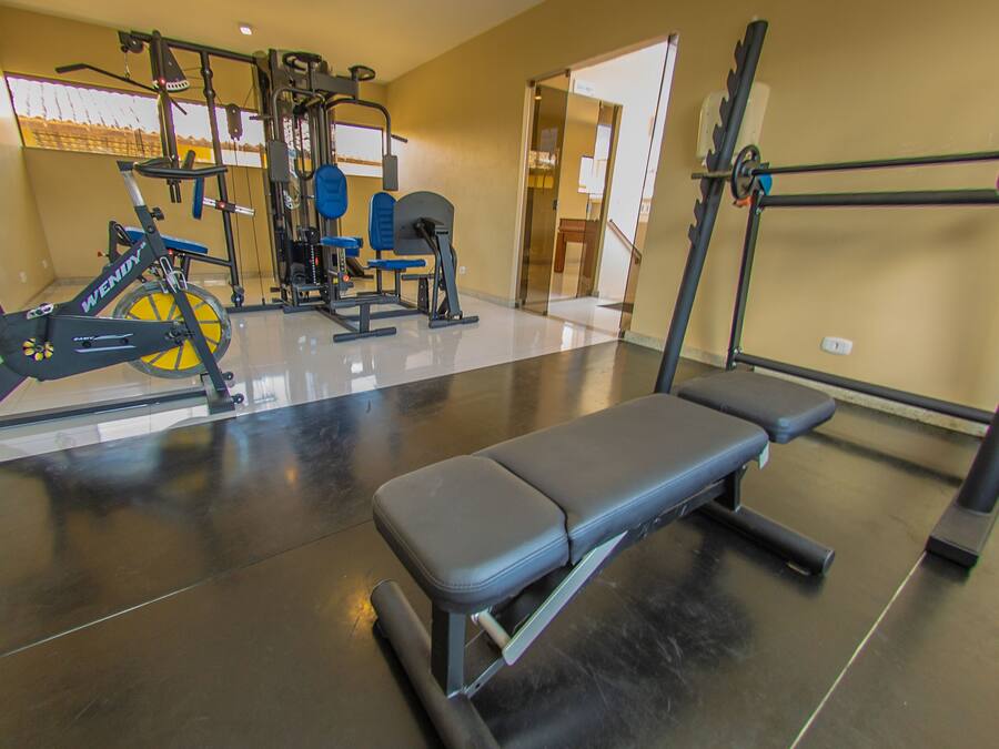 Academia com equipamentos de ginástica, um banco e um espelho.