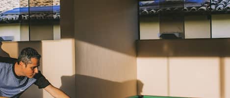 A pool table with balls, a person playing, and a television mounted on the wall.