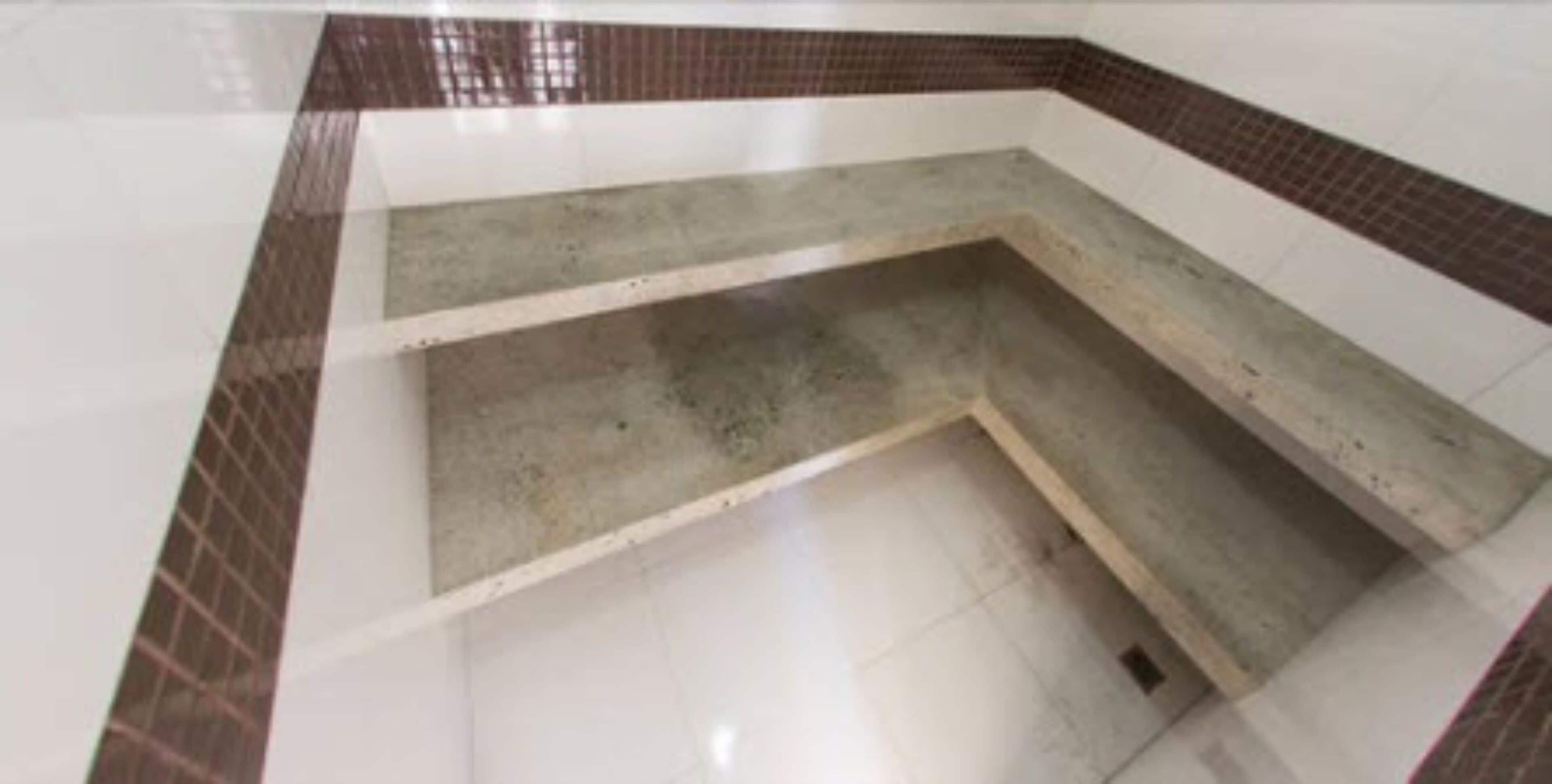 A bathroom with a tiled floor, a concrete bench, and a corner sink.