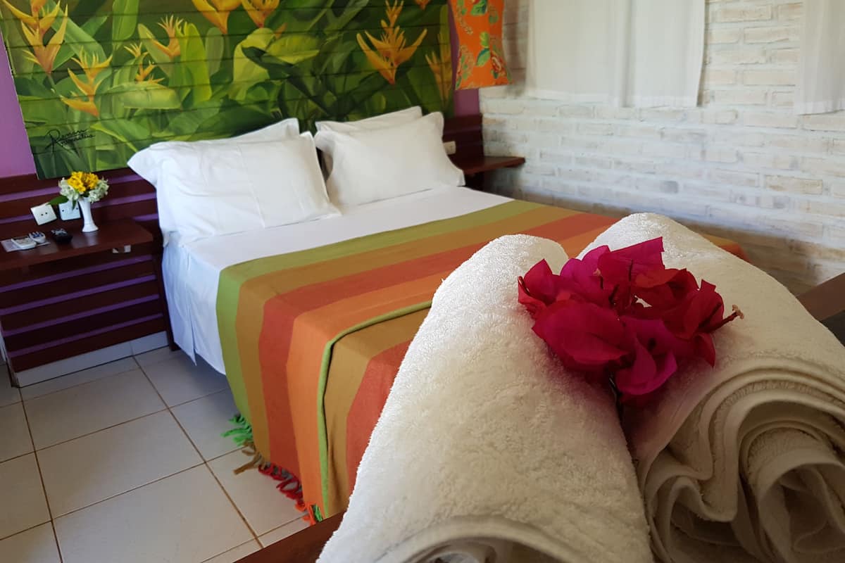 A hotel room with a bed, a nightstand with a vase of flowers, a colorful striped blanket, and a headboard with a floral mural.