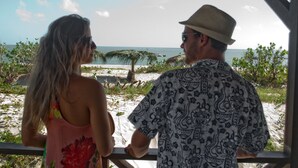 Ein Paar blickt auf einen Strand mit einem Gebäude mit einem Reetdach.