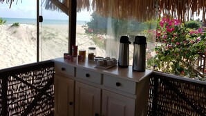 Ein Zimmer mit Blick auf den Strand, einem Reetdach und einem Tisch mit Küchenutensilien.