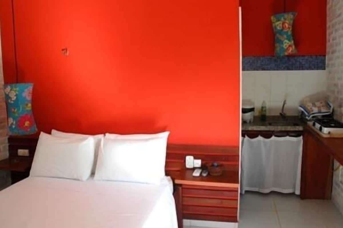 A hotel room with a large bed, a wooden nightstand, a small table with a telephone, and a bathroom visible through an open door.