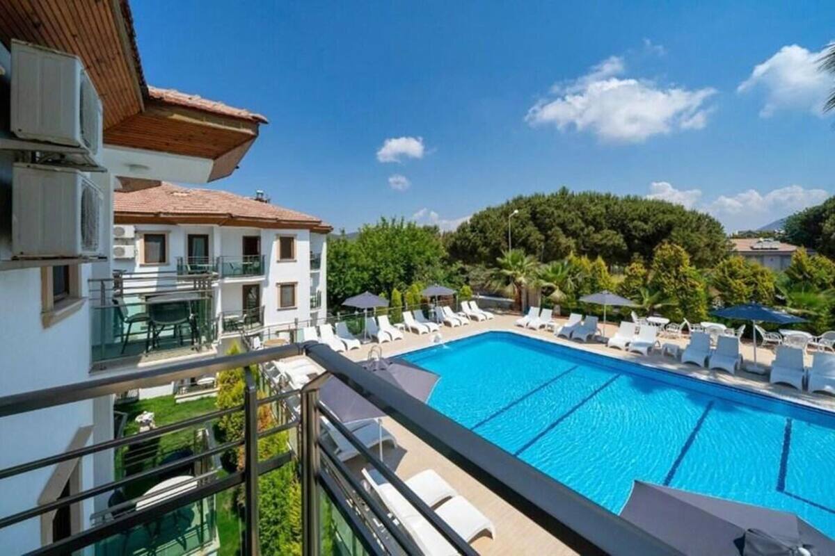 A swimming pool with lounge chairs and umbrellas, surrounded by greenery and buildings.