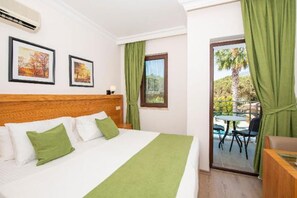 A hotel room with a bed, green curtains, a window with a view, and a balcony with a table and chairs.