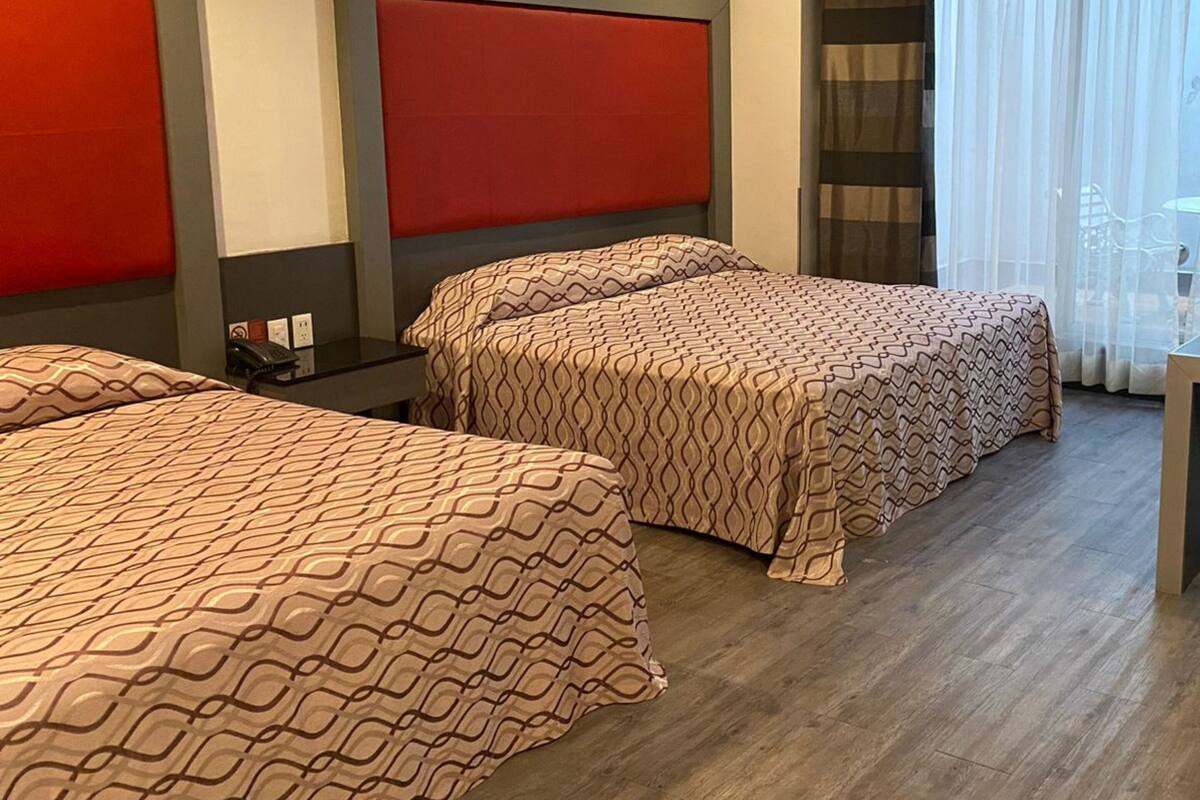 Une chambre d’hôtel avec deux lits, un mur d’accent rouge, un ventilateur de plafond et une vue sur l’extérieur.