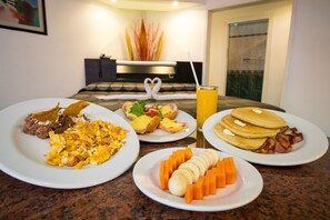 Un buffet de petit-déjeuner proposant des œufs brouillés, du bacon, des crêpes et des fruits frais présentés sur des assiettes.